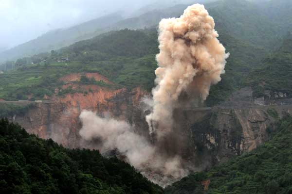 A controlled explosion erupts on Thursday to remove hazardous rocks near a barrier lake formed by continuous rainfall in Sanjiao, Sichuan Province. More blasts will follow to carve out a flood channel and discharge the floodwater.