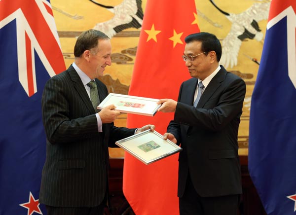 Premier Li Keqiang (R) and New Zealand Prime Minister John Key exchange sample banknotes at a ceremony in the Great Hall of the People in Beijing on Tuesday. They announced that the two countries have approved direct trading between their currencies. [Photo/China Daily]