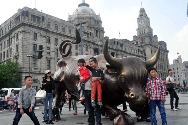 Tourists pose beside the bronze statue of a charging bull on the Bund in Shanghai early this month. [Photo/China Daily] 