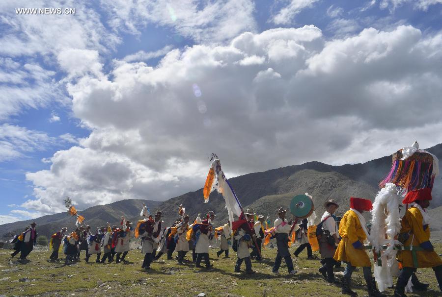 Farmers in holiday array carry scriptures while attending an Ongkor Festival prayer ceremony in Bomtoi Village, Dagze County, Lhasa, southwest China's Tibet Autonomous Region, July 1, 2014. By walking around farmlands, villagers of the Tibetan ethnic group pray for good harvests during the annual Ongkor Festival, or Bumper Harvest Festival.