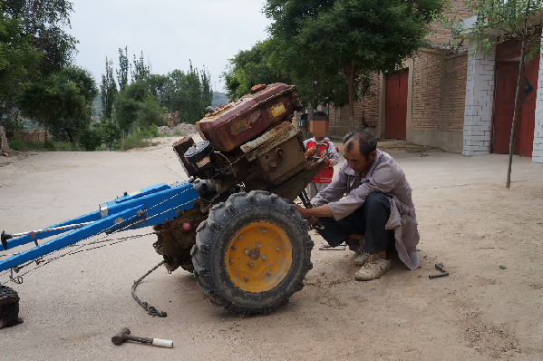 A farmer (front) in Daping Village, Dingxi, Gansu Province is preparing a tractor. A large number of young farmers have left countryside to cities and towns for higher-paid jobs, leaving only the elderly and children in the village. [China.org.cn By Wu Jin]