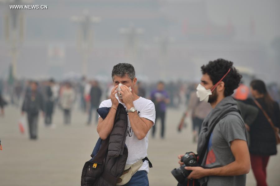 A foreign tourist (L) adjusts his mask as visiting the smog-shrouded Tian'anmen Square in Beijing, capital of China, Oct. 9, 2014.