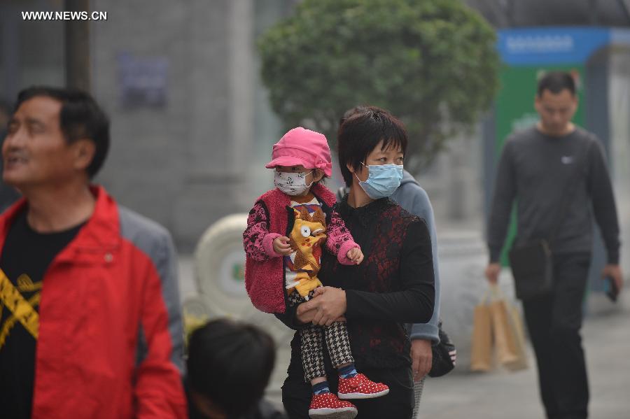 A woman holding a child walk in the Qianmen Street in smog-shrouded Beijing, capital of China, Oct. 9, 2014.