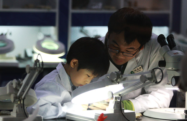 Shang Yiyang, right, volunteers at the Paleozoological Museum of China in Beijing teaching children fossil repairing, March 29, 2015.[Photo by Song Wei/chinadaily.com.cn] 