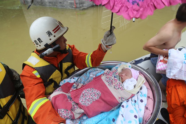 A rescuer escorts a sleeping 10-month-old infant to safety on Tuesday in Xiaba, a village in Guizhou province that has been left submerged by consecutive heavy downpours. [Photo/China Daily]