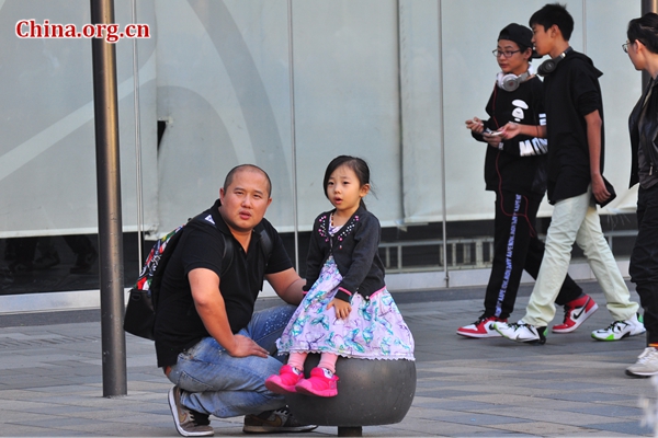 A little girl sits on a stone in Sanlitun, Beijing‘s Eastern Chaoyang District, accompanied by her parent in early spring. [Photo by Guo Yiming / China.org.cn]